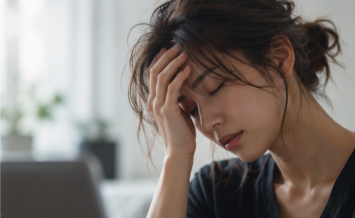 額に手を当て、疲れた表情で目を閉じる女性