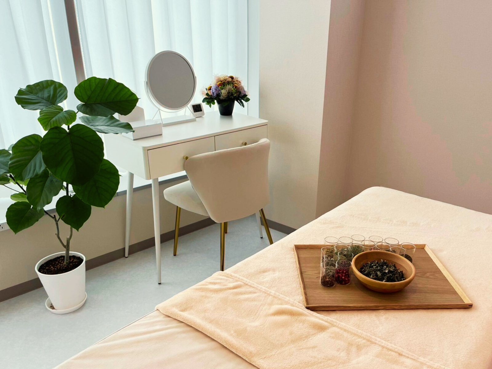 白を基調にした明るい施術ルーム。窓際の鏡台と観葉植物、ベッドの上にはハーブティーの茶葉